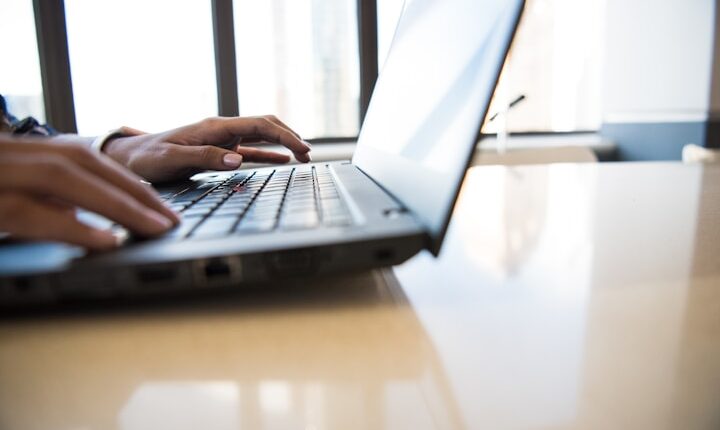 person using black laptop on brown table